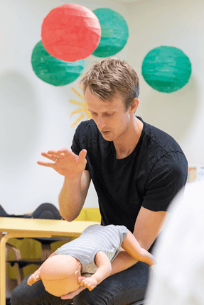 En man ger HLR träning med en Little Baby QCPR, mörk hud, docka för första hjälpen i klassrumsmiljö.