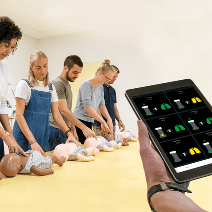 Grupp som övar på Little Baby QCPR mörk hud docka med hjälp av en surfplatta för HLR-träning.