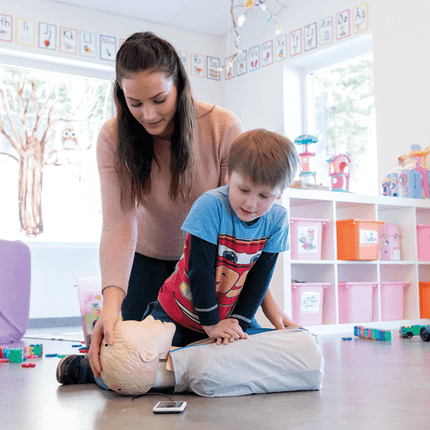 HLR-docka för barn med väska som används av en vuxen och ett barn i lekfull miljö.